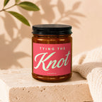 Brown glass candle with pink label reading "TYING THE Knot" and "VOWED".
