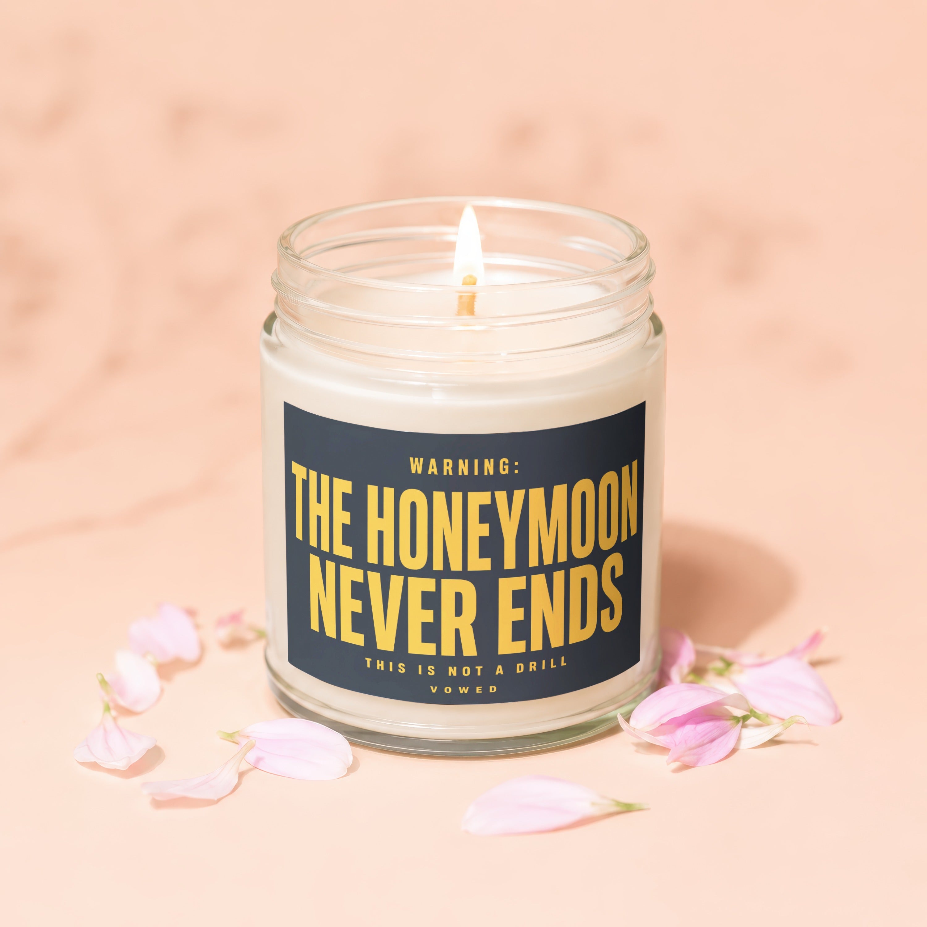 Lit candle in a jar with "The Honeymoon Never Ends" text, surrounded by petals.