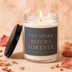Glass jar candle lit with "THE SPARK BEFORE FOREVER" text on label, with lid ajar.