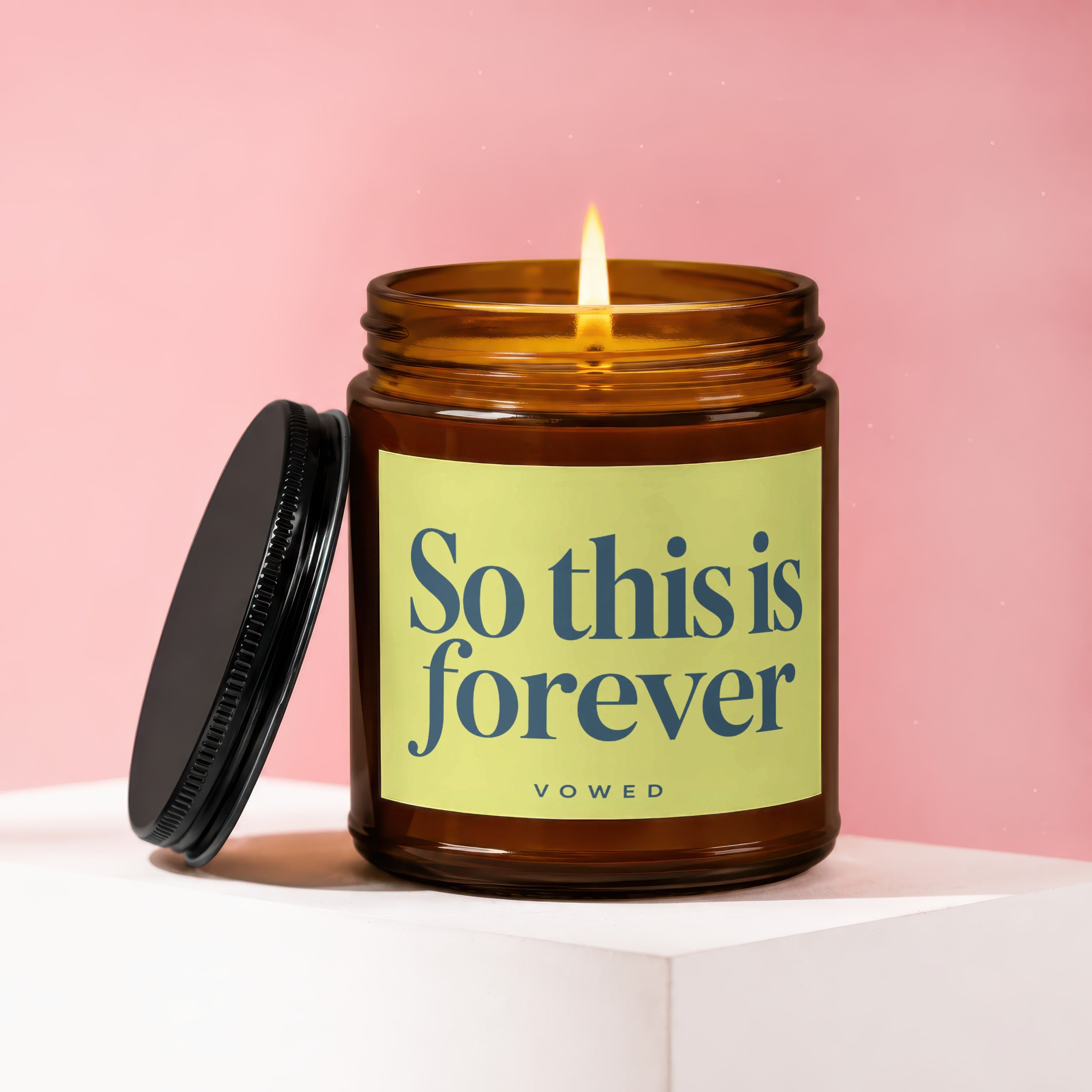 Candle with lit wick and an open black lid, label says "So this is forever VOWED".
