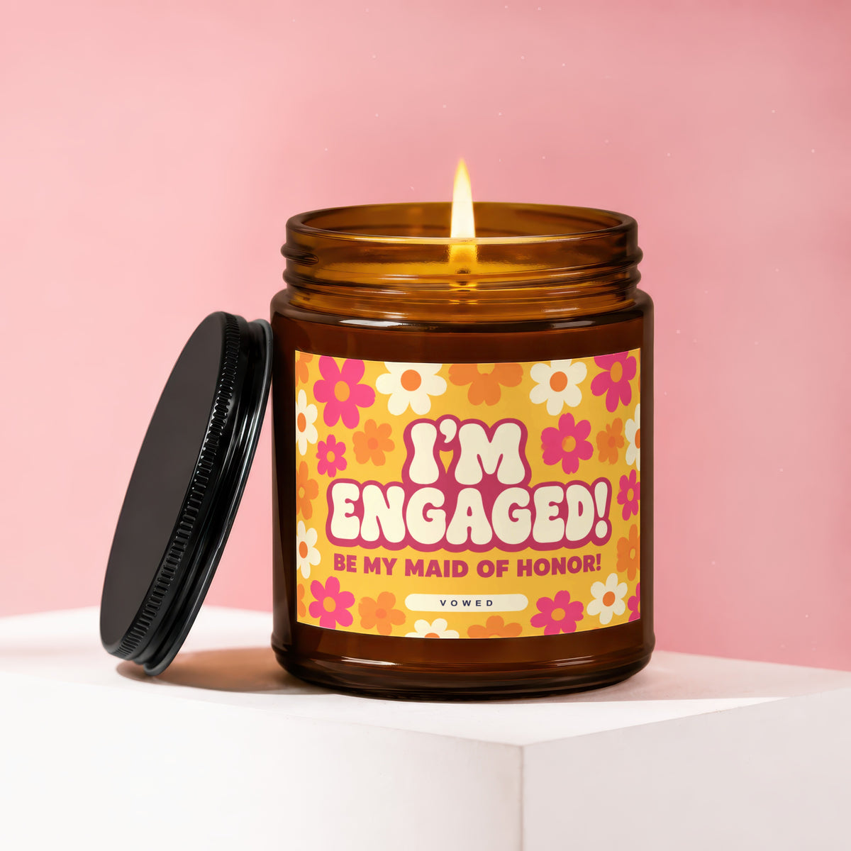 Amber candle with lit wick and flower pattern label saying "I'm Engaged! Be My Maid of Honor!".