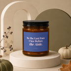 Amber candle with blue label reading "Be the Last Face I See Before the Aisle."