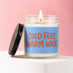 Glass jar candle with lit wick and lid, featuring "COLD FEET, WARM WICK" label.