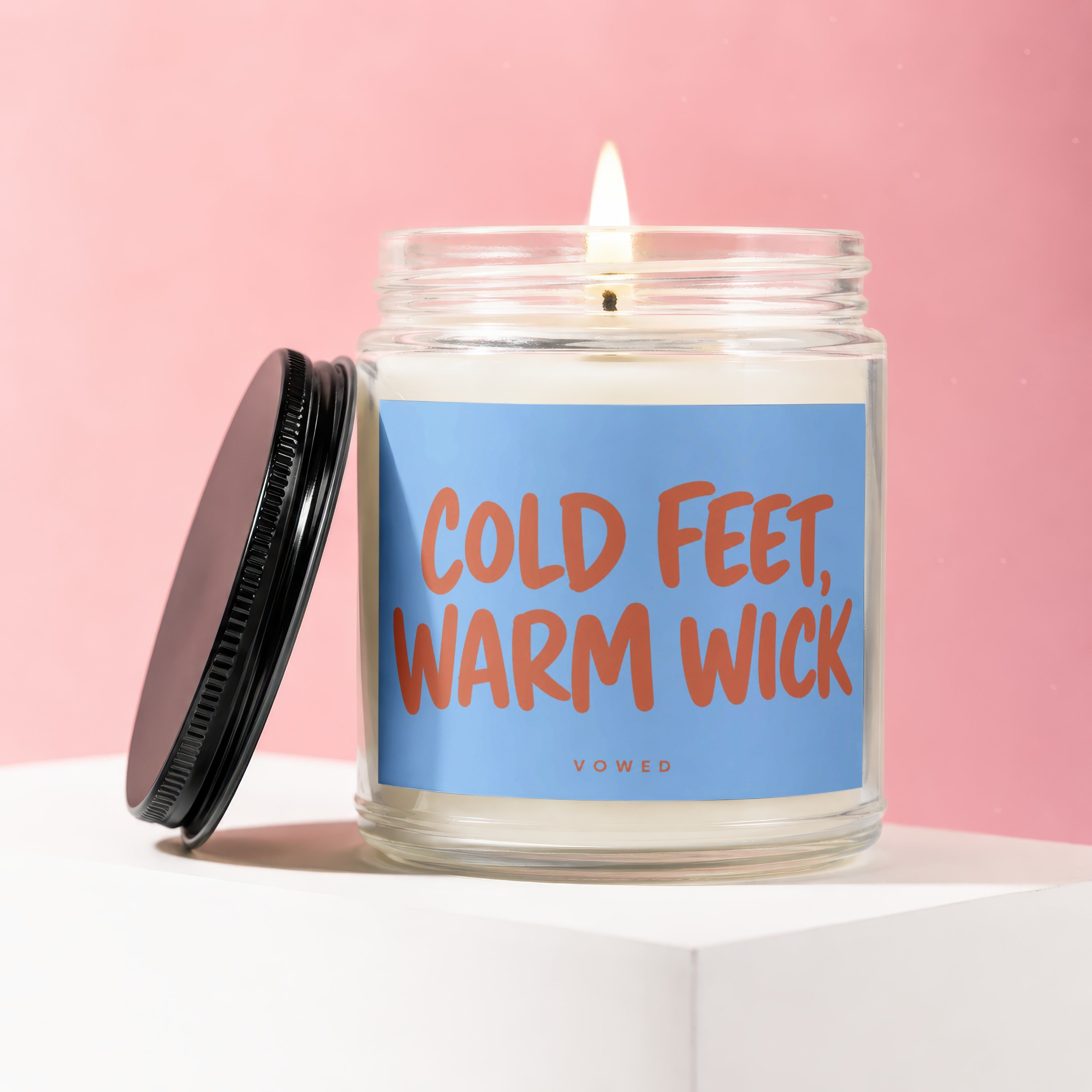 Glass jar candle with lit wick and lid, featuring "COLD FEET, WARM WICK" label.