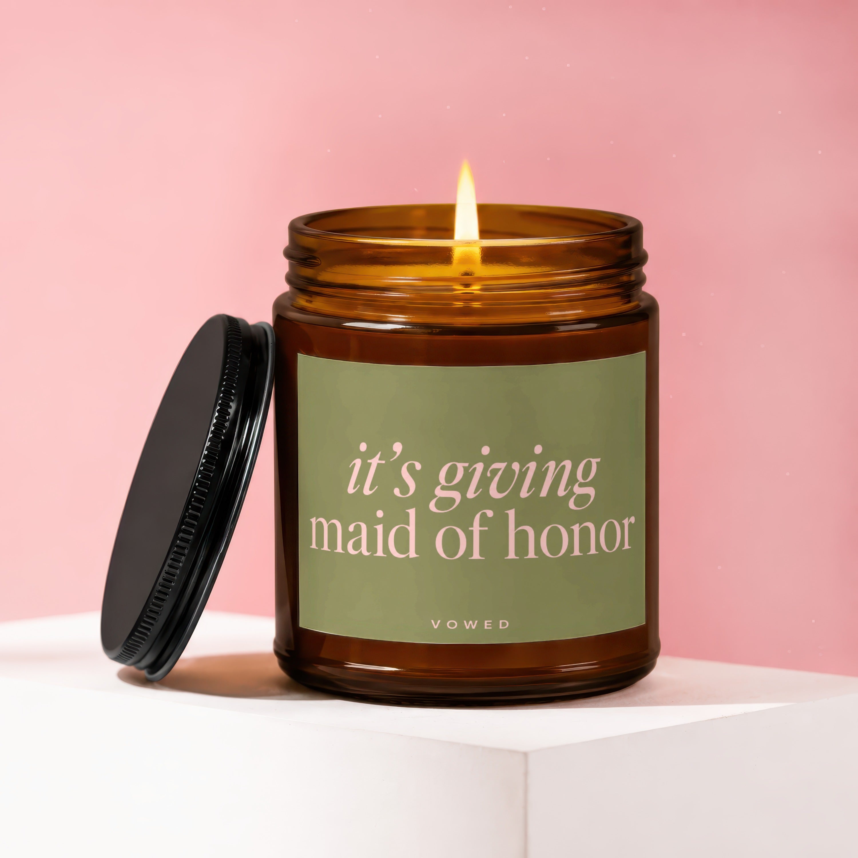 Amber glass candle with lit wick, lid off, and "it's giving maid of honor" text.