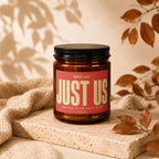 Amber candle with black lid and red label reading "JUST US"