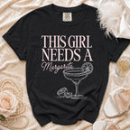 Black t-shirt with "This Girl Needs a Margarita" text and margarita graphic.