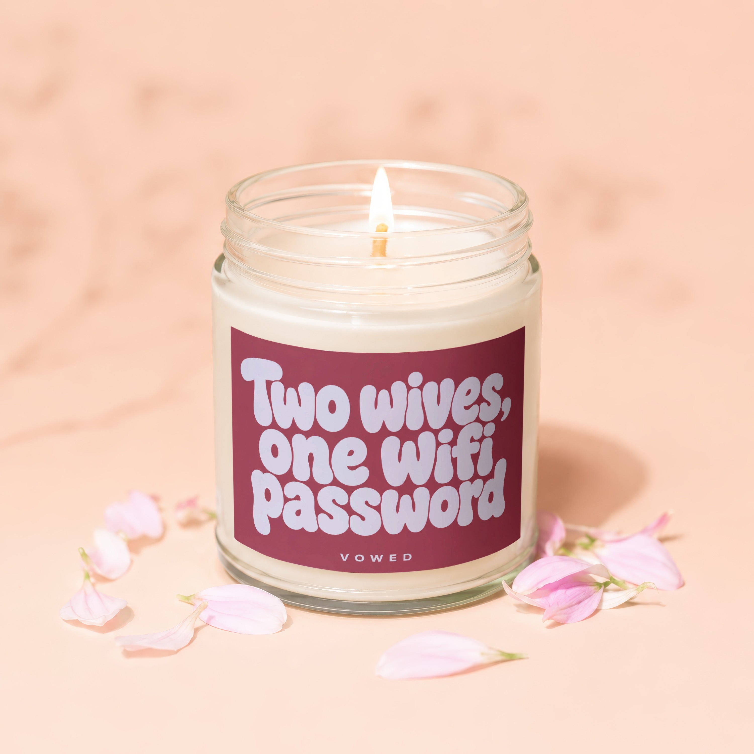 Lit candle in a jar with "Two wives, one wifi, password" text, surrounded by flower petals.