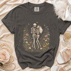 Dark gray t-shirt with a graphic of skeletons in a floral meadow wearing wedding attire.