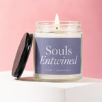 Scented candle labeled "Souls Entwined" with lid off, lit wick, on a white pedestal.
