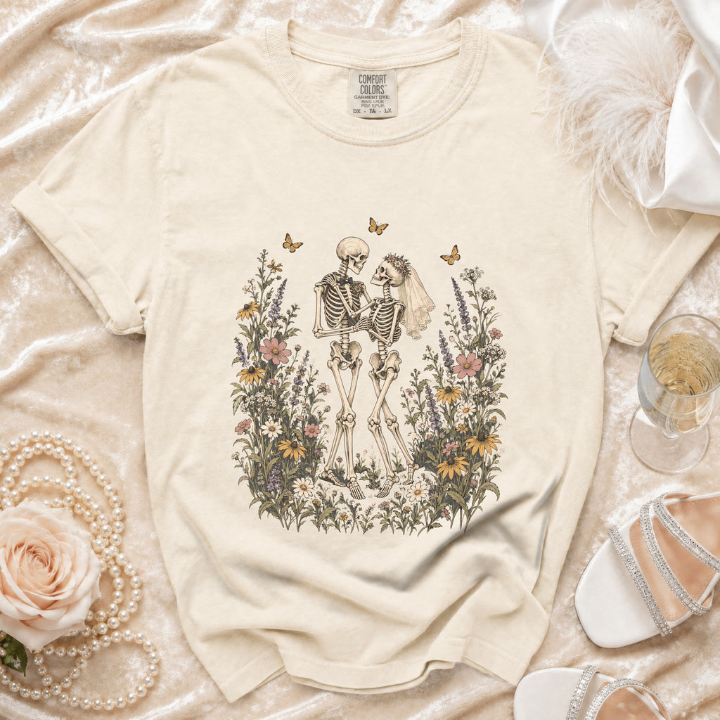 Skeleton couple in wedding attire surrounded by wildflowers and butterflies on a cream t-shirt.