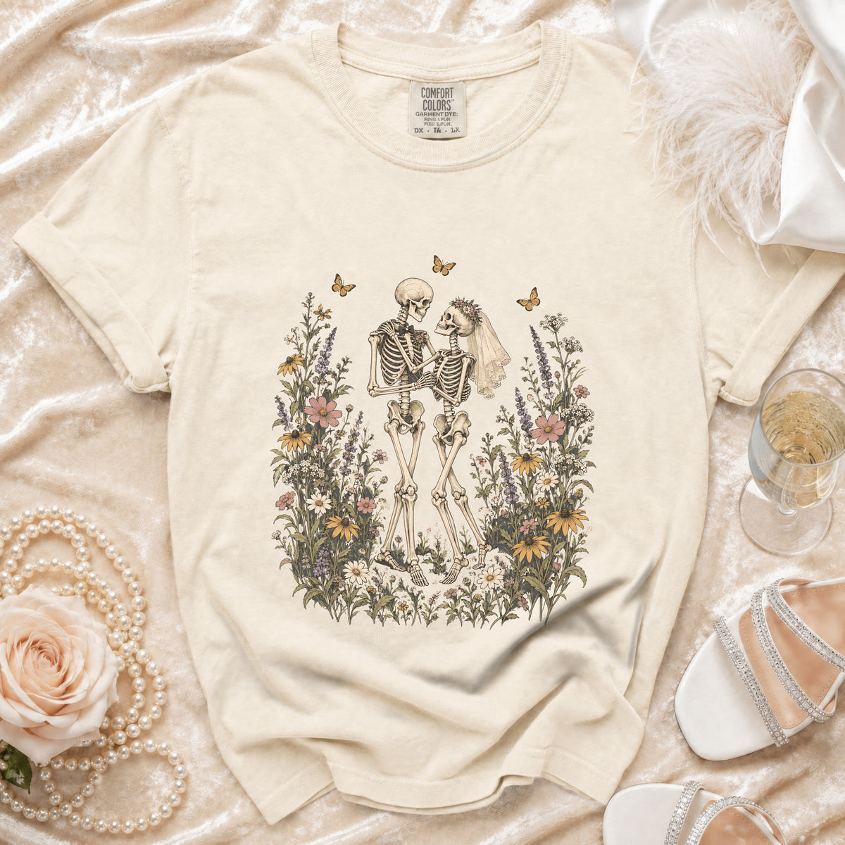 Skeleton couple in wedding attire surrounded by wildflowers and butterflies on a cream t-shirt.