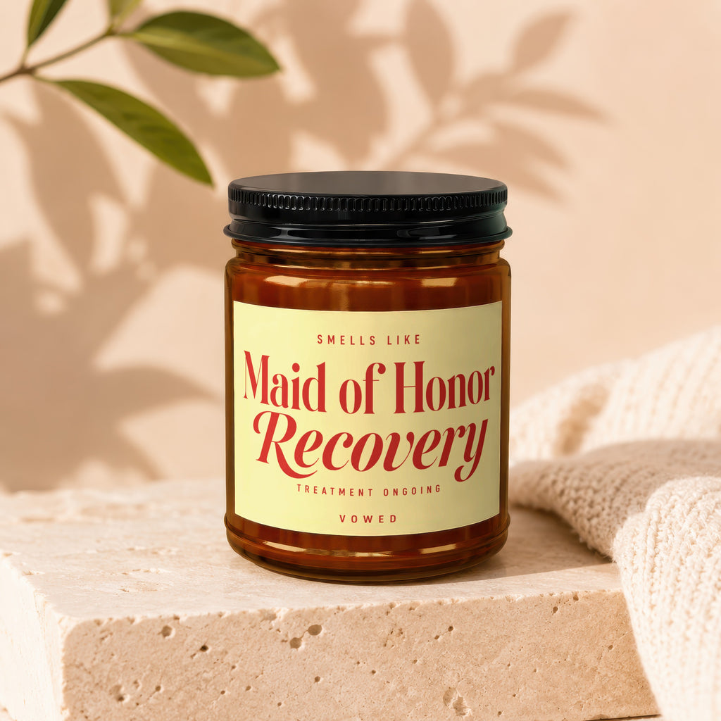Brown glass jar candle with "Maid of Honor Recovery" text, black lid, on stone.