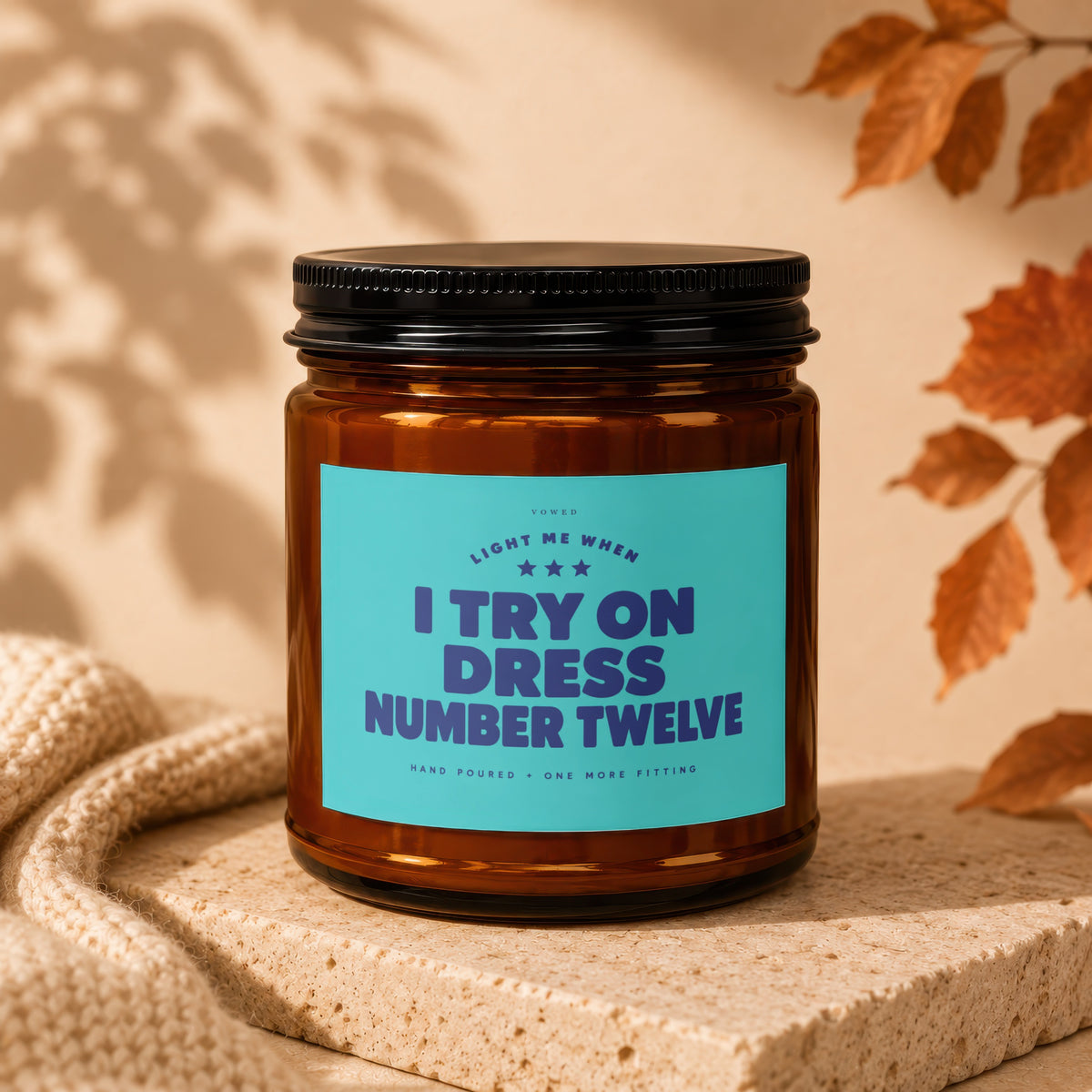 Brown glass candle with teal label reading "I TRY ON DRESS NUMBER TWELVE".