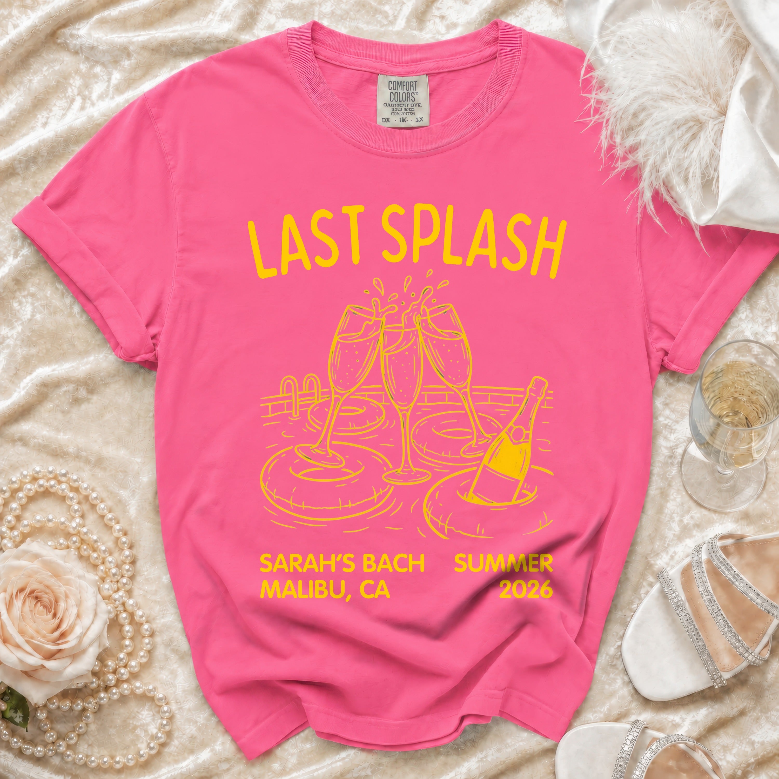 Pink t-shirt with "Last Splash" text, champagne glasses, pool floats, and bottle.
