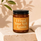 Amber jar candle with orange label reading "I Fixed Your Veil. Again. VOWED."