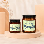 Two amber glass candles labeled "Smells Like Official Hype Girl" are displayed.
