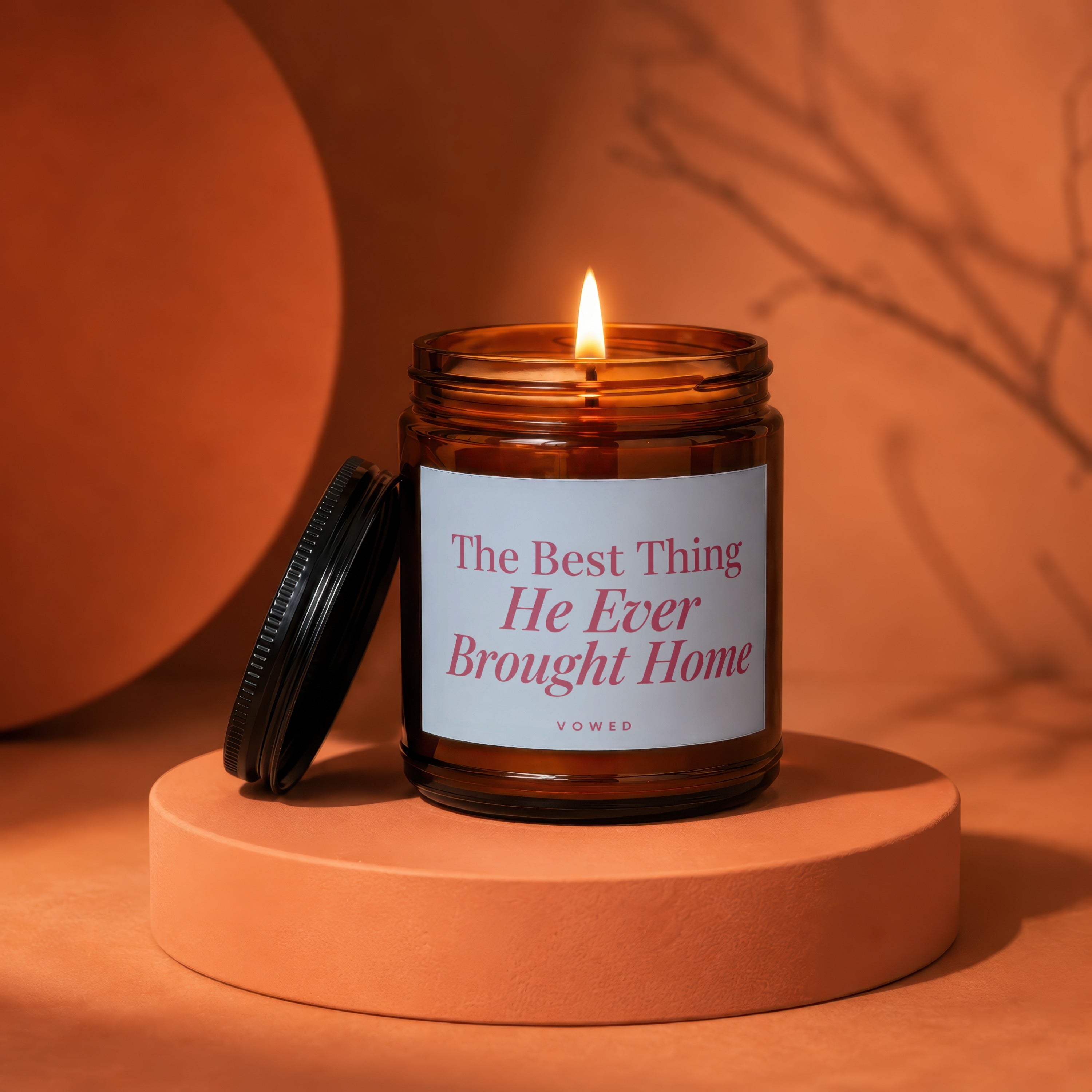 Amber jar candle with lit flame and text "The Best Thing He Ever Brought Home vowed".