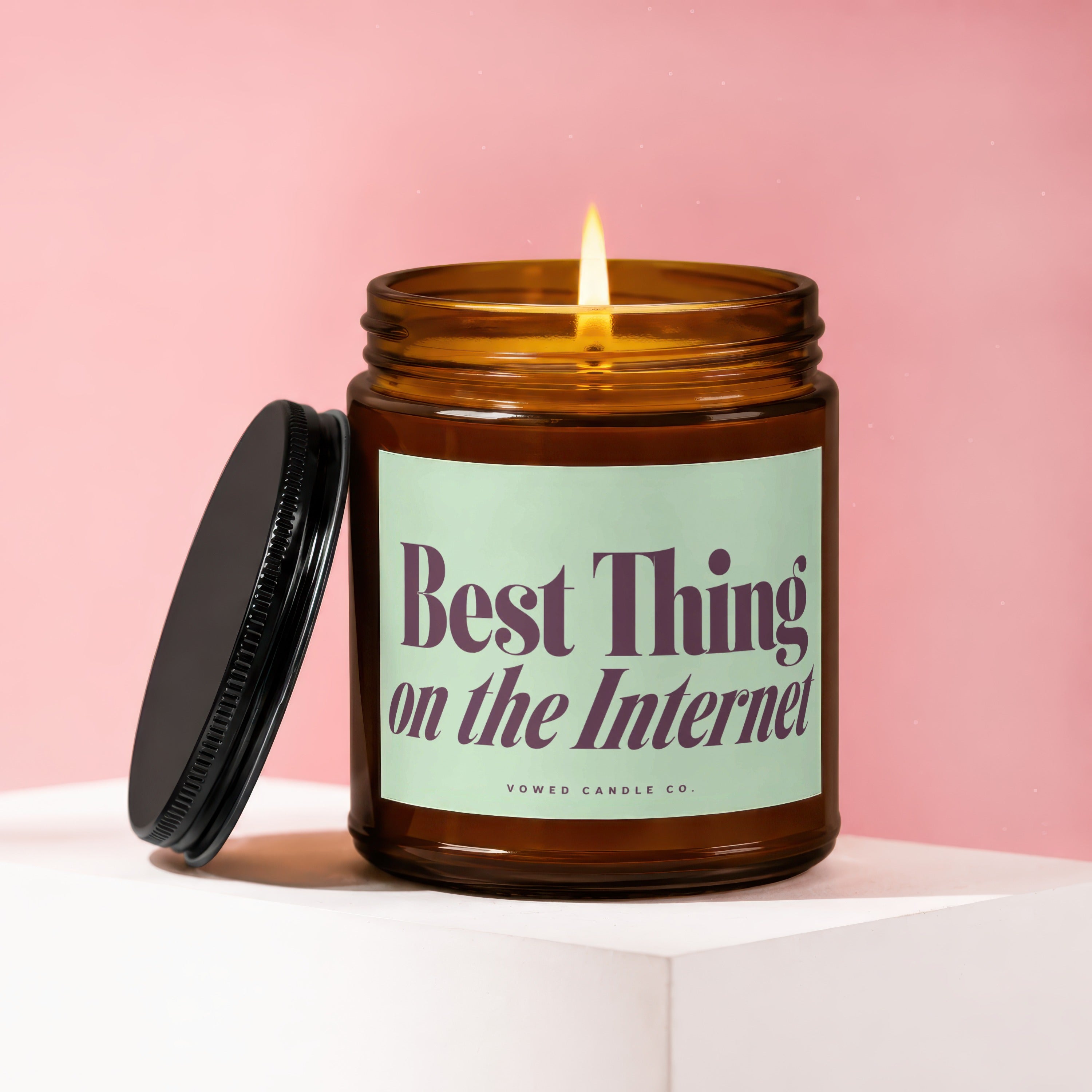 Amber candle with lit flame, "Best Thing on the Internet" text, and black lid.