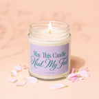 Glass jar candle with lit wick on a pink surface with pink petals.