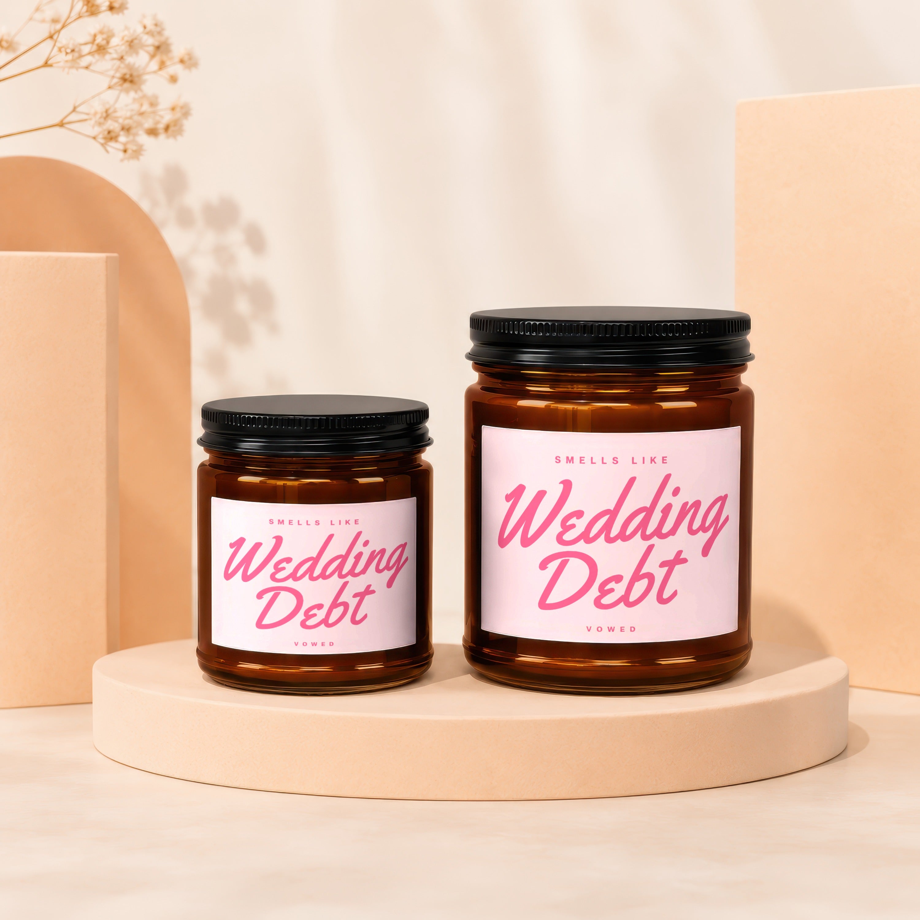 Two amber glass candles with "Wedding Debt" text and black lids on display pedestals.