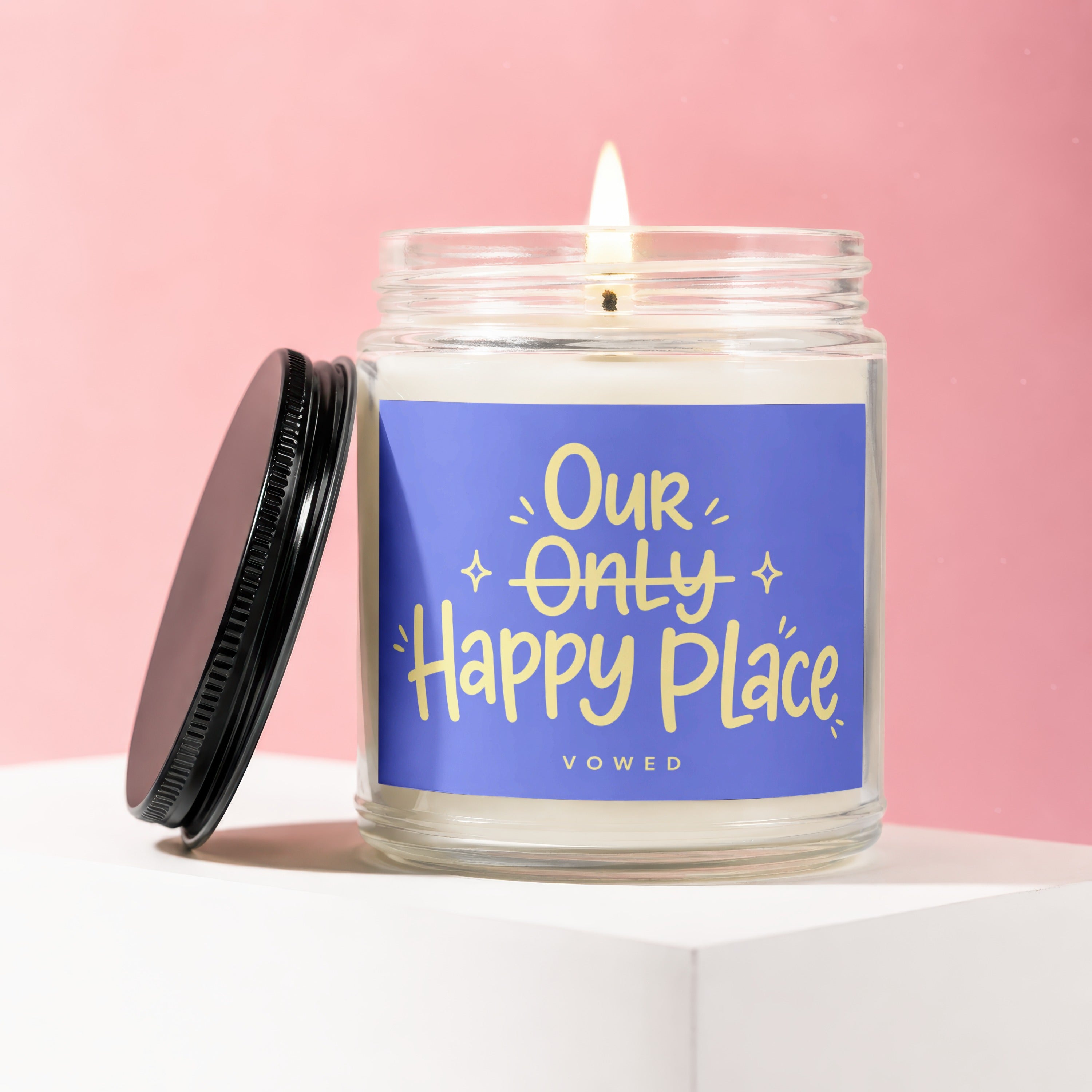 Jar candle with lit flame and lid off, reading "Our Only Happy Place VOWED".