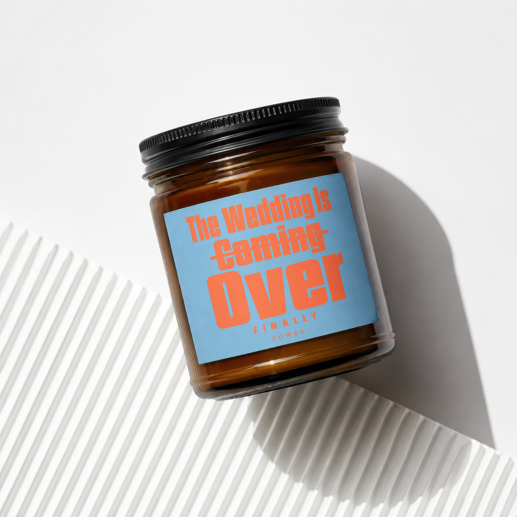 Amber jar candle with black lid, light blue label reads "The Wedding Is Coming Over Finally Vowed".