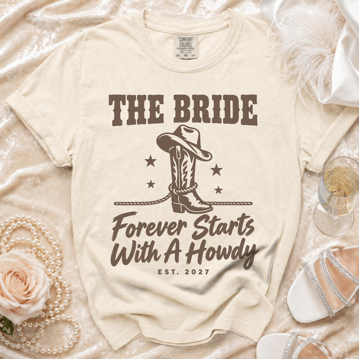 Cream t-shirt featuring brown text reading "The Bride Forever Starts With A Howdy" and a cowboy boot graphic.