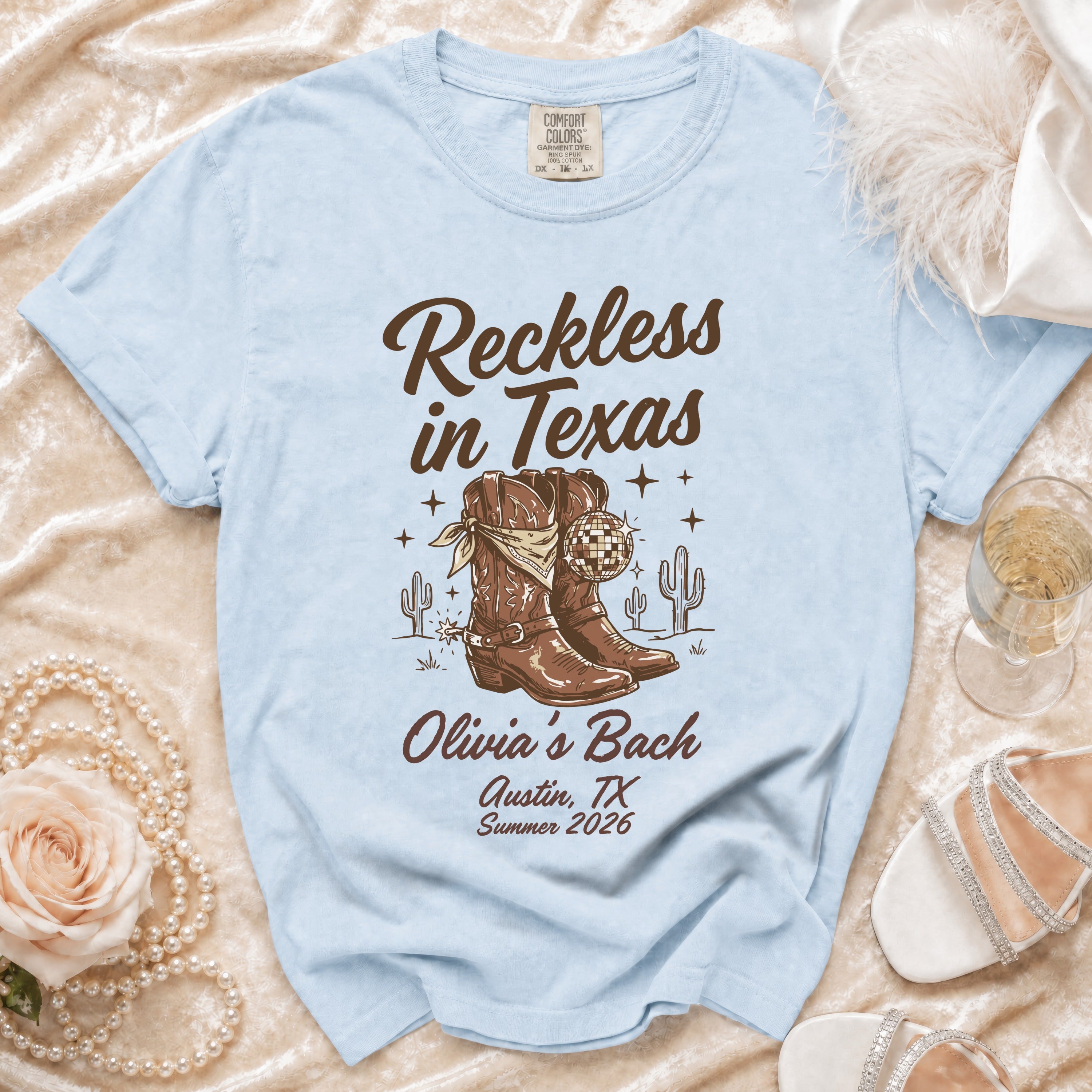 Light blue t-shirt with "Reckless in Texas" and cowboy boot graphic.