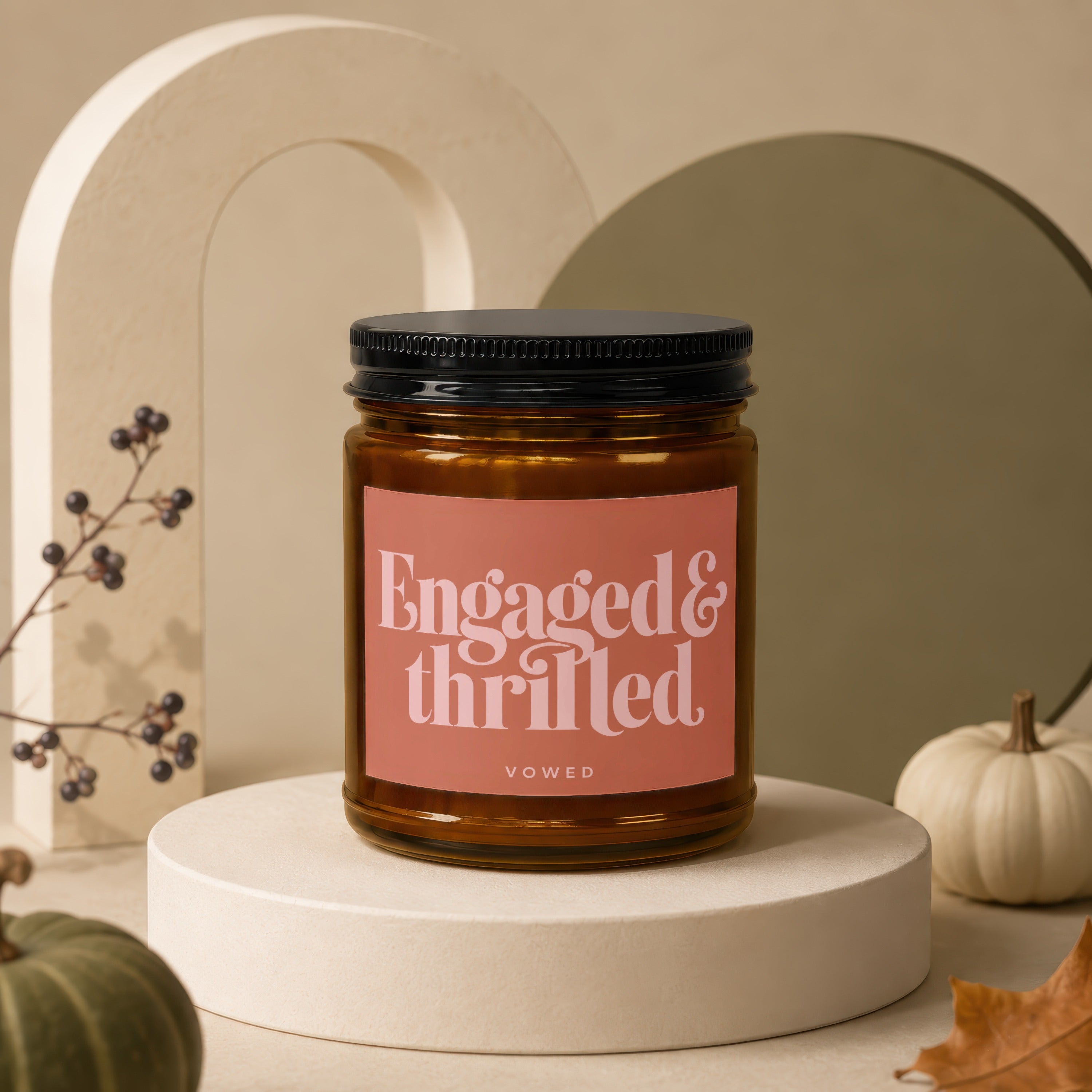 Candle labeled "Engaged & Thrilled" by VOWED on a pedestal with autumn decor.