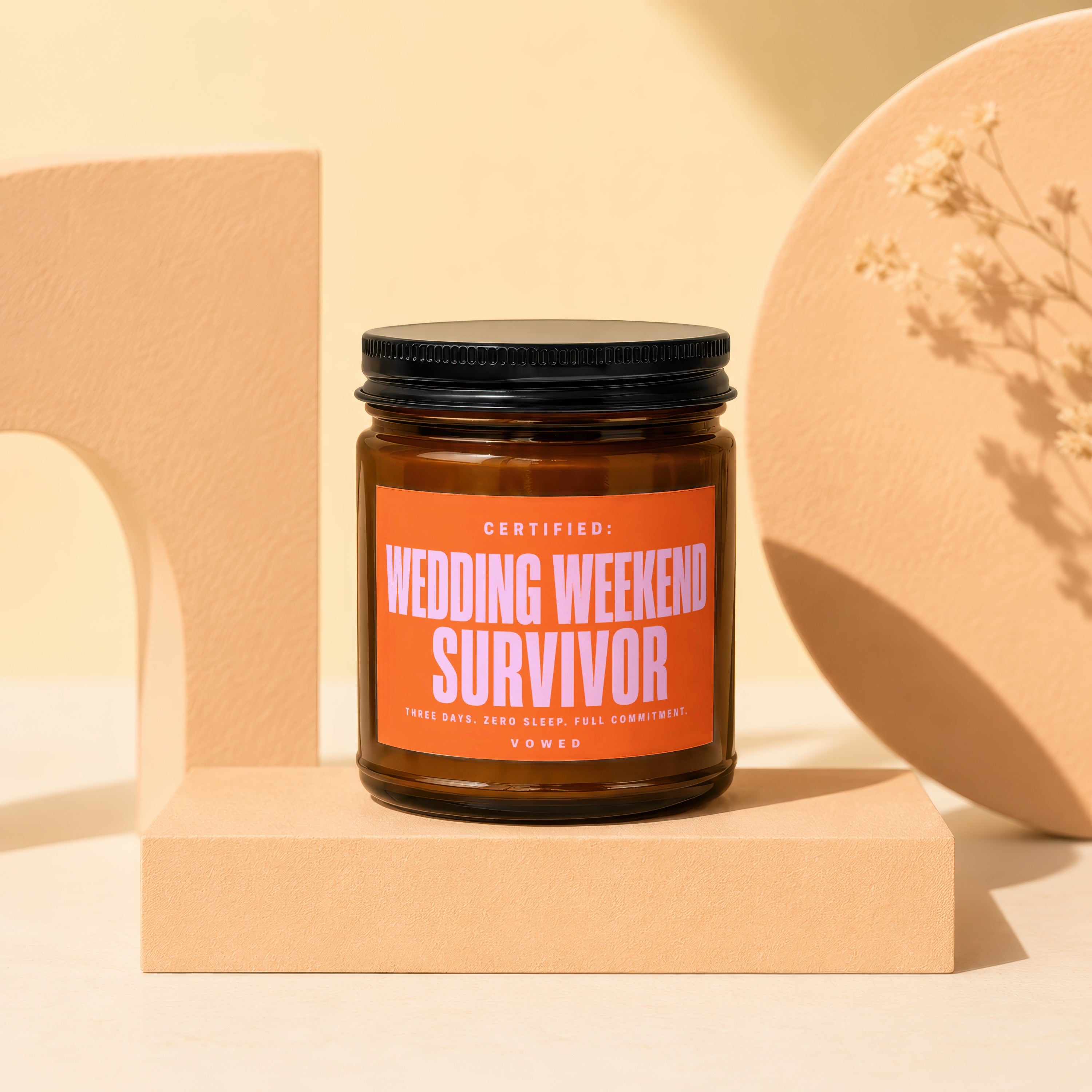 Brown candle in amber glass jar with orange label reading "Wedding Weekend Survivor".