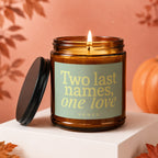Amber candle with lit wick, lid off, and text "Two last names, one love VOWED".