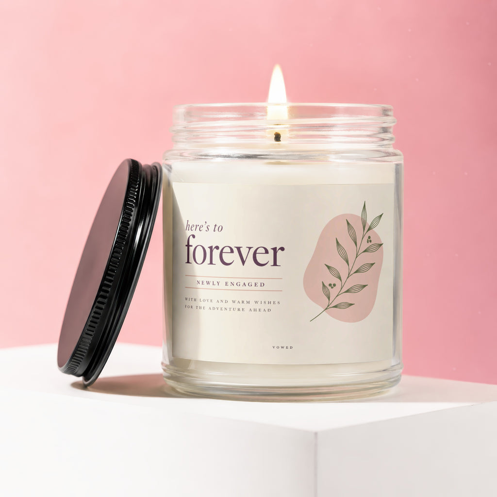 Candle with "here's to forever" and "newly engaged" text on a pink background.