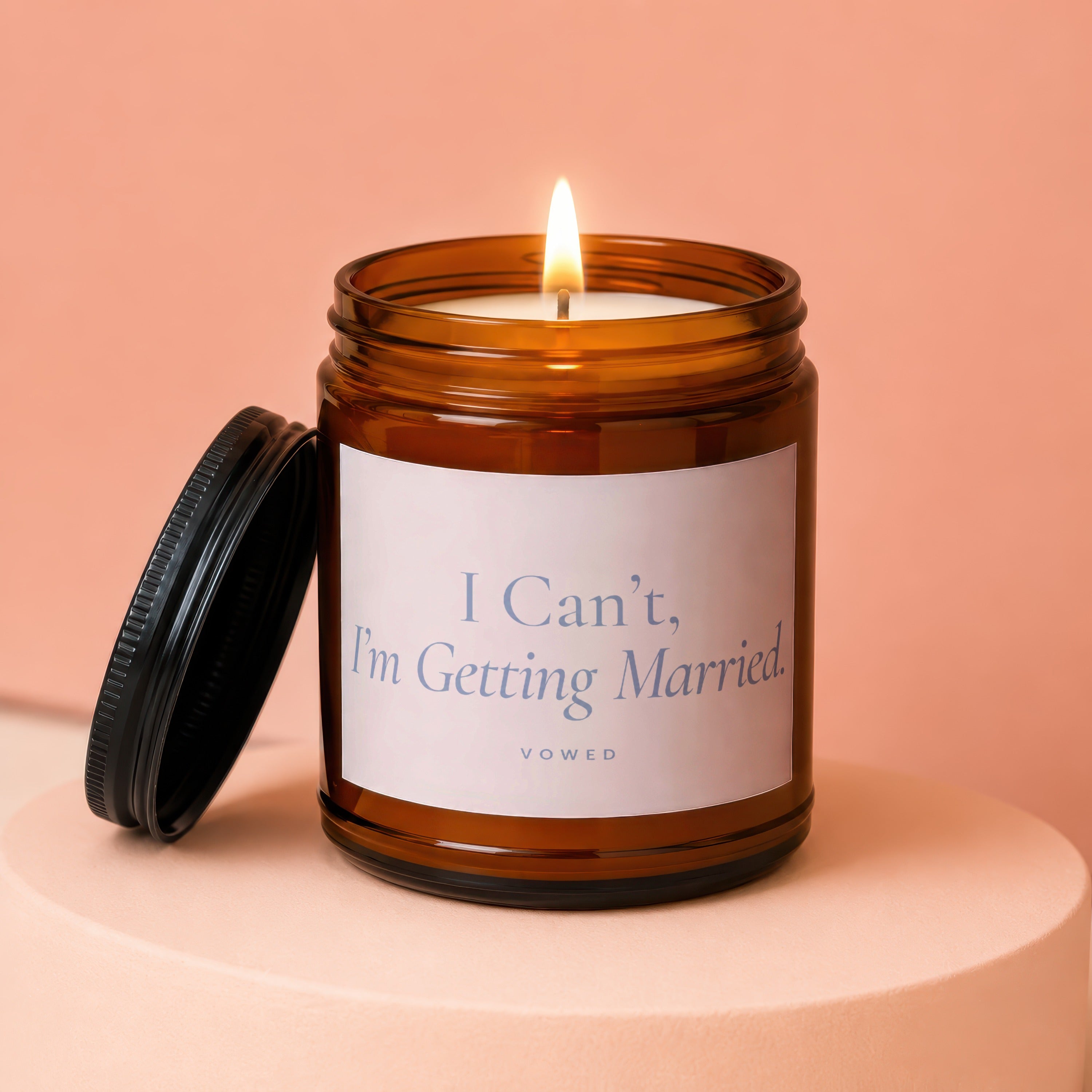 Amber jar candle with lit flame and lid off, reads "I Can't, I'm Getting Married. VOWED."