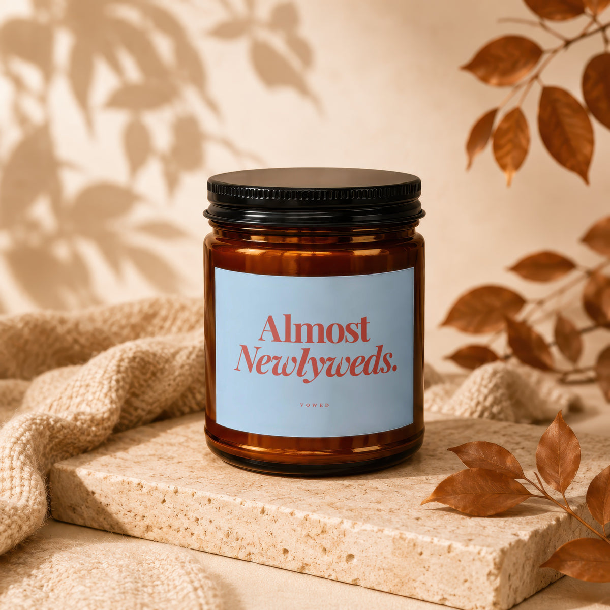 Amber candle with black lid, "Almost Newlyweds" label, on textured stone.