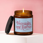Lit amber glass candle with lid off, has a light blue label with pink text.