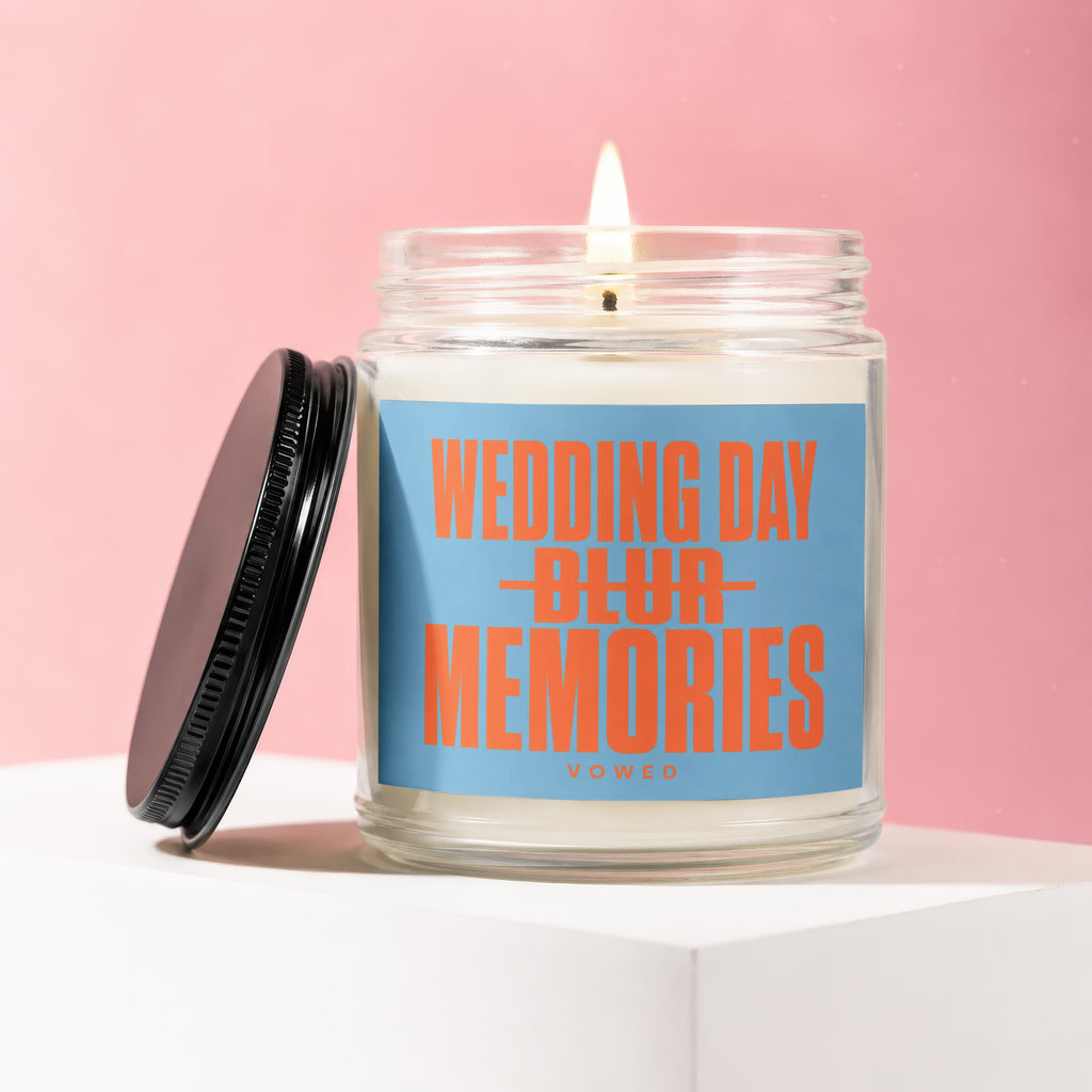 Candle with lid ajar, featuring a blue label with orange text "WEDDING DAY BLUR MEMORIES VOWED".