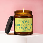 Amber glass candle with lit flame and black lid, reads "FROM GIRLFRIENDS TO WIVES".