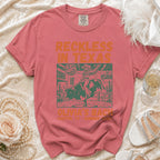 Coral t-shirt with "Reckless in Texas" and bull riding graphic.