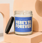 Glass candle with blue label reading "RAISE A GLASS: HERE'S TO FOREVER AND EVERY ORDINARY TUESDAY IN IT VOWED".