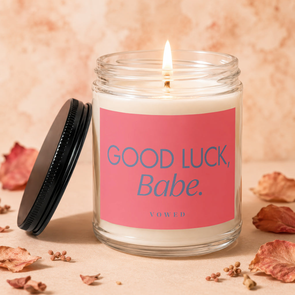 Candle with lit wick, pink label reading "GOOD LUCK, Babe. VOWED".