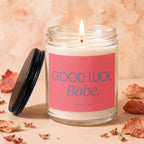 Candle with lit wick, pink label reading "GOOD LUCK, Babe. VOWED".