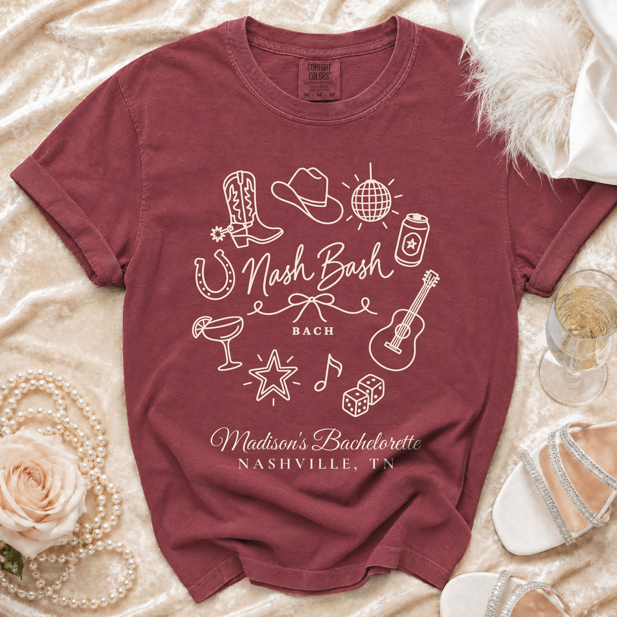 A maroon short-sleeve t-shirt with white outline graphics and text reading Nash Bash and Madison's Bachelorette Nashville TN.