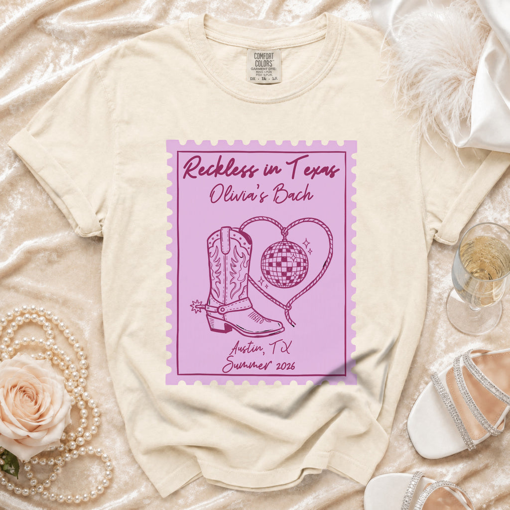 Cream t-shirt with "Reckless in Texas" stamp design, cowboy boot, disco ball, and text.