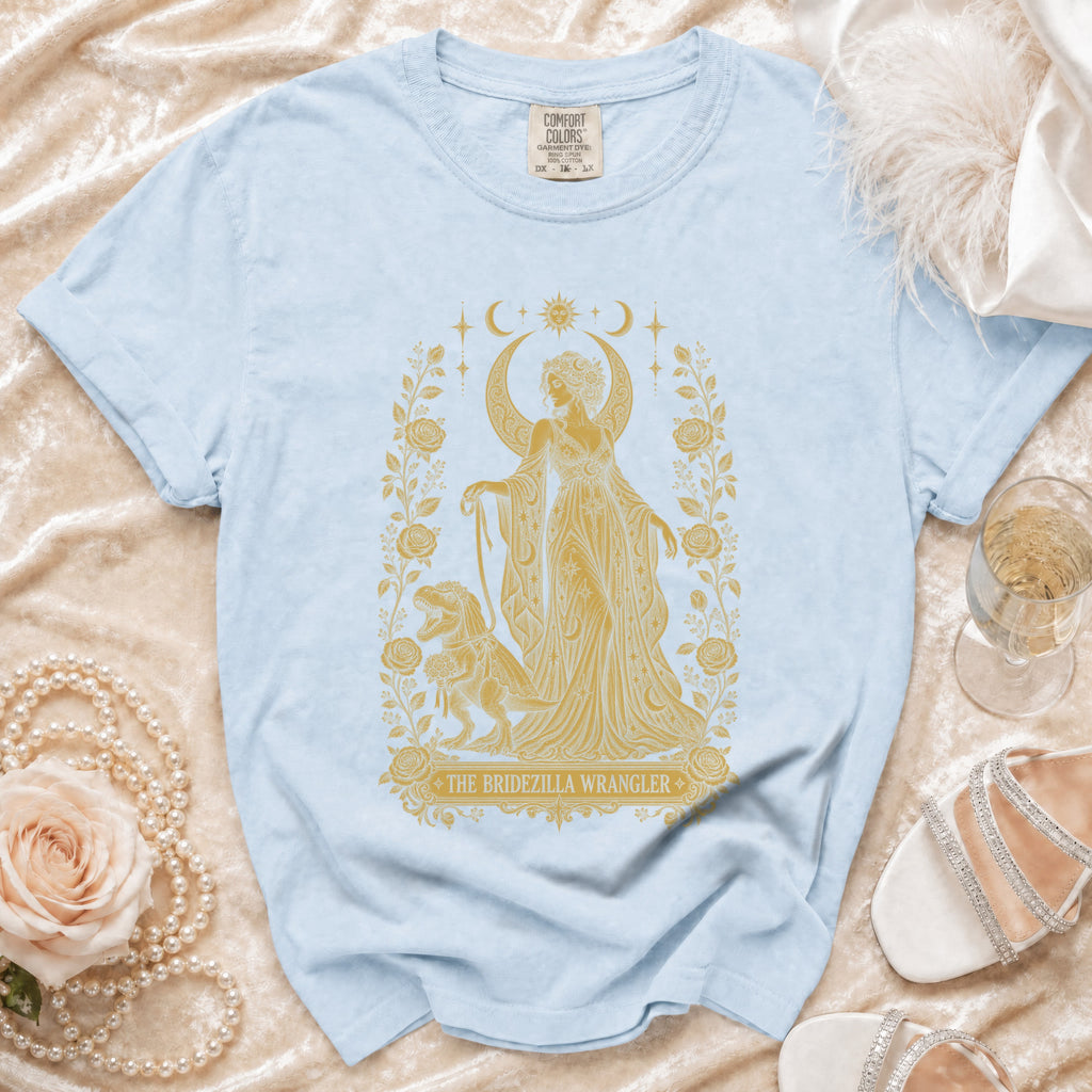 Light blue t-shirt with golden "The Bridezilla Wrangler" graphic of woman and dinosaur.