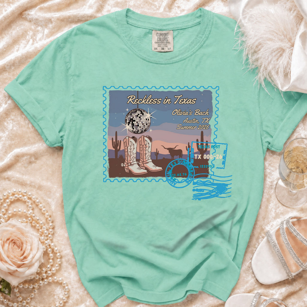 Teal t-shirt with "Reckless in Texas" design featuring boots, disco ball, and Austin details.
