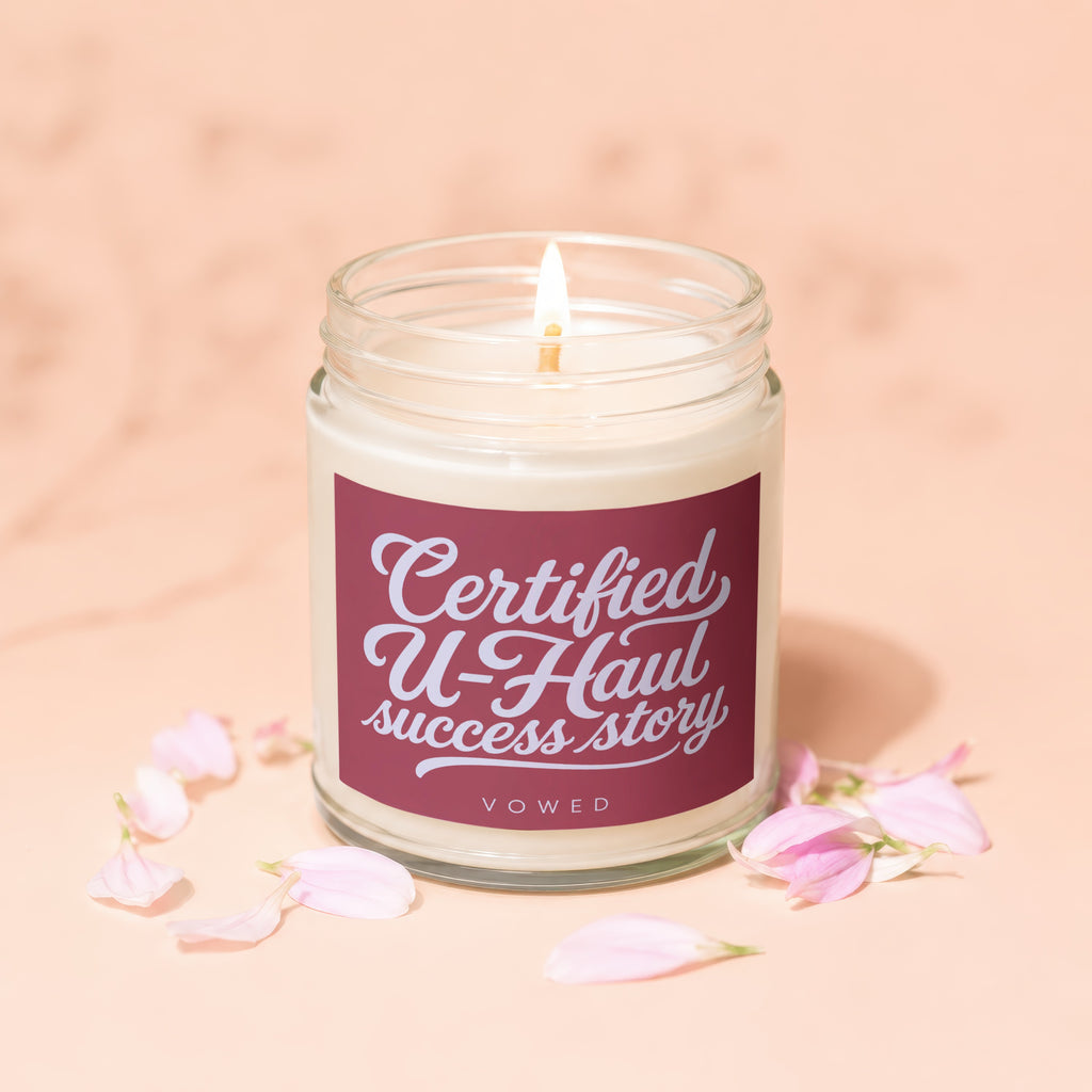 Glass jar candle with burgundy label reading "Certified U-Haul success story" and "VOWED".
