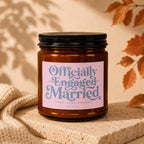 Amber jar candle with pink label reading "Officially Engaged Married Took Long Enough Vowed".