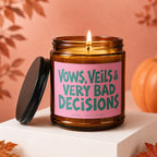 Amber jar candle with burning flame and pink label: "Vows, Veils & Very Bad Decisions."