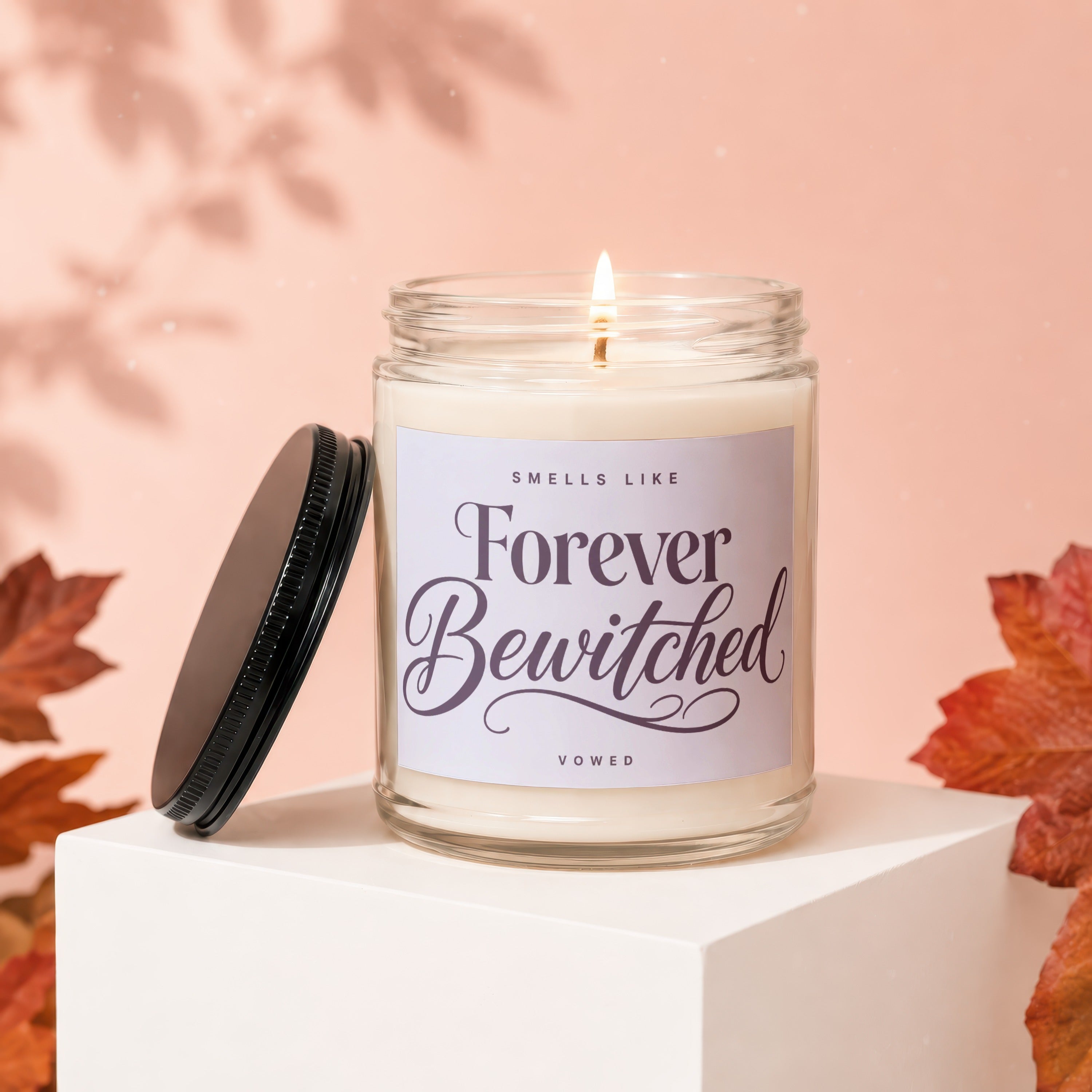 Lit candle in glass jar with "Smells Like Forever Bewitched" label on pink background.